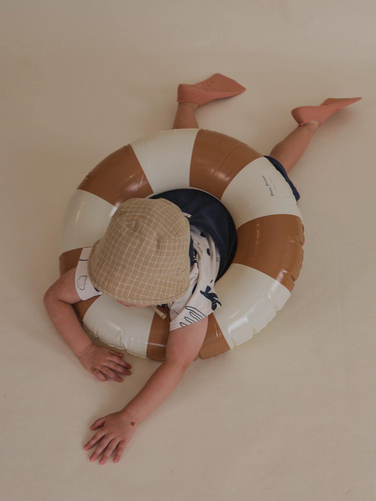 toddler wearing wheat gold muslin bucket hat with grid lines, pretend play swimming with pool ring & flippers