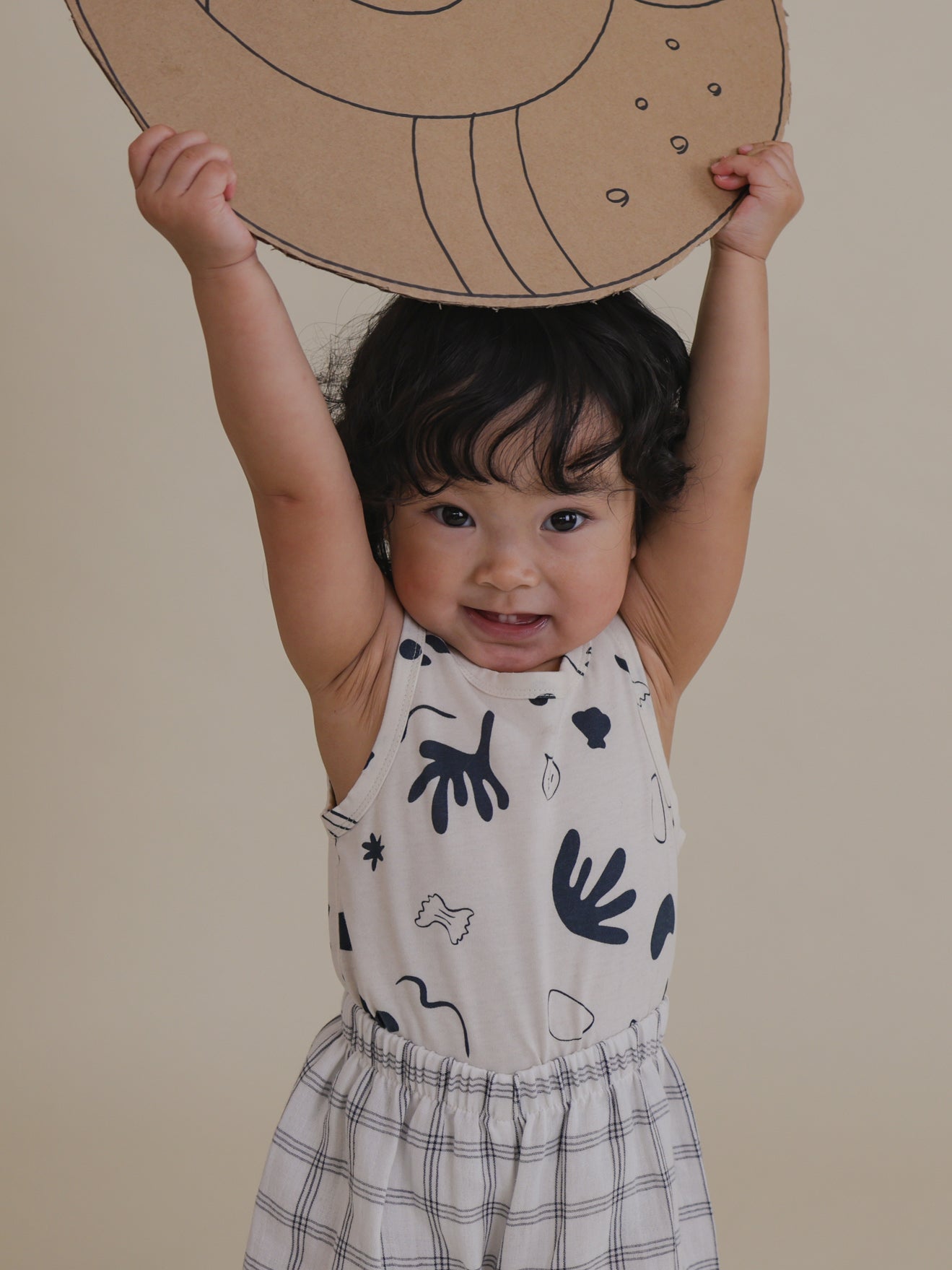 toddler in capri summer vest with navy ocean print tucked in pants holding cardboard cutout above head