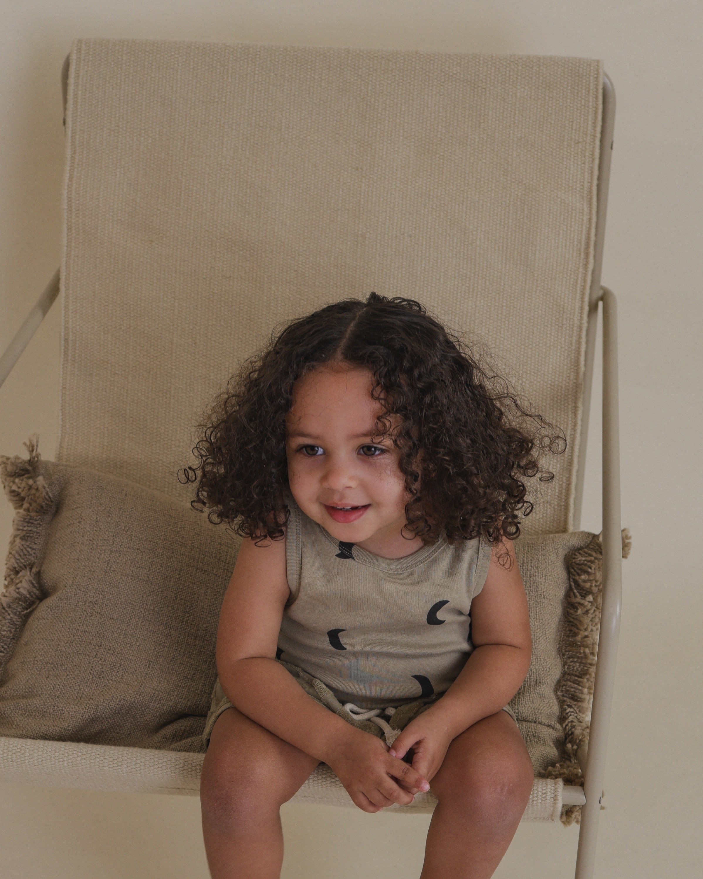 toddler in dusky beige summer vest with black moon print lounging on chair