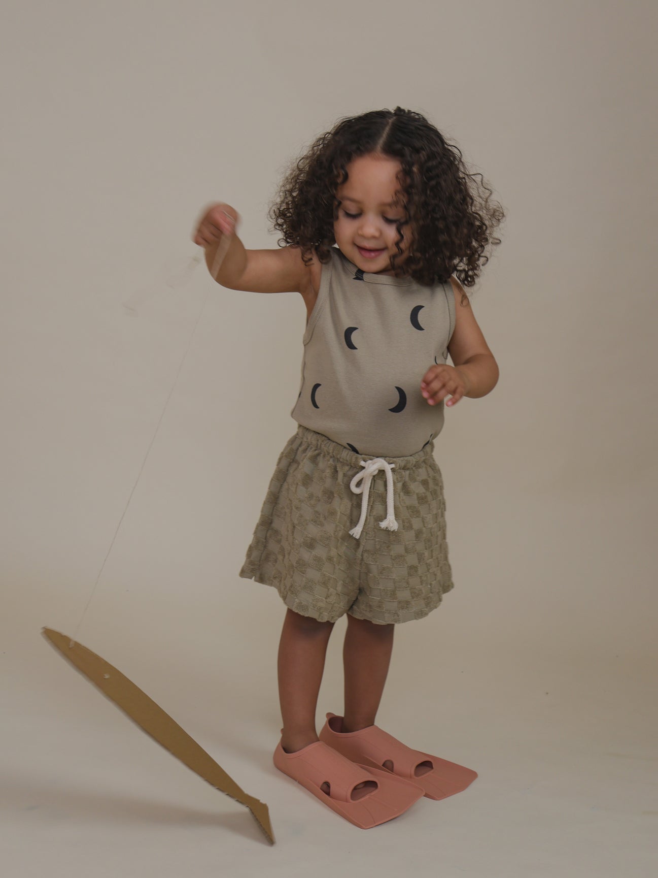 toddler wearing beige vest with moon print & checkerboard rope shorts pretend play fishing