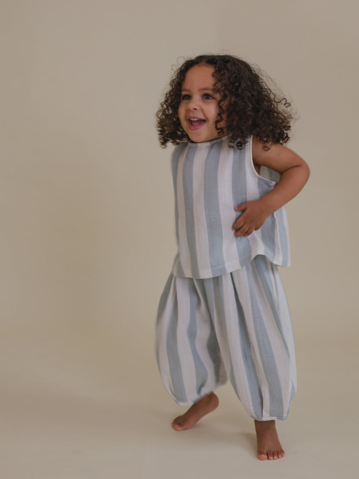 toddler jumping in matching sardine blue striped sleeveless muslin ribbon-tie top & trousers