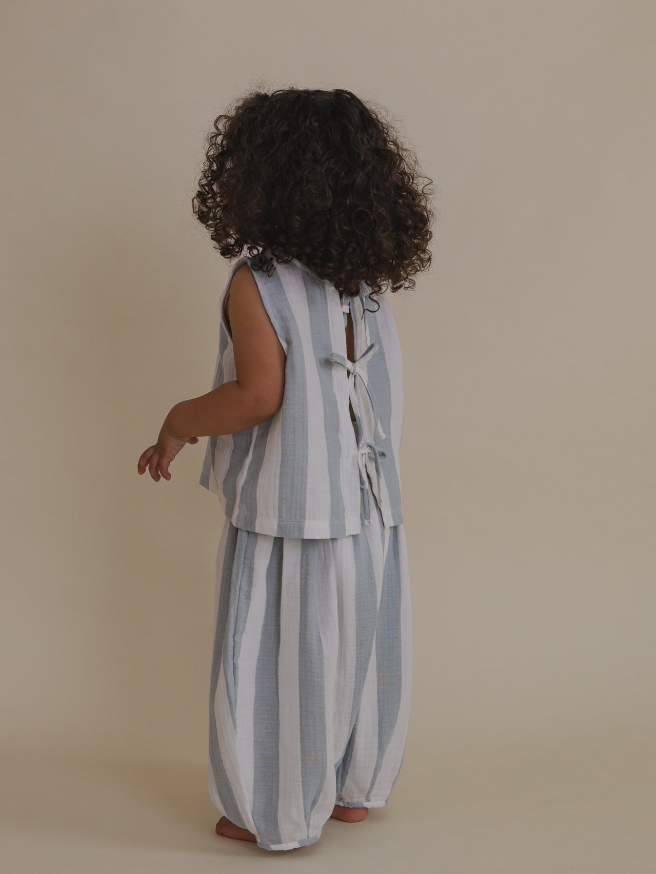 toddler wearing matching blue striped sleeveless muslin ribbon-tie back top & trousers
