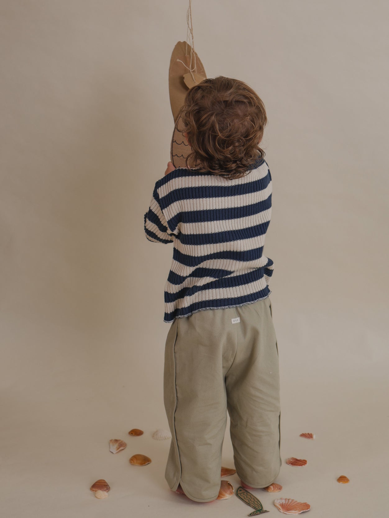 back view of toddler in seasalt grey balloon pants & stripes sweater, playing with cardboard fishes