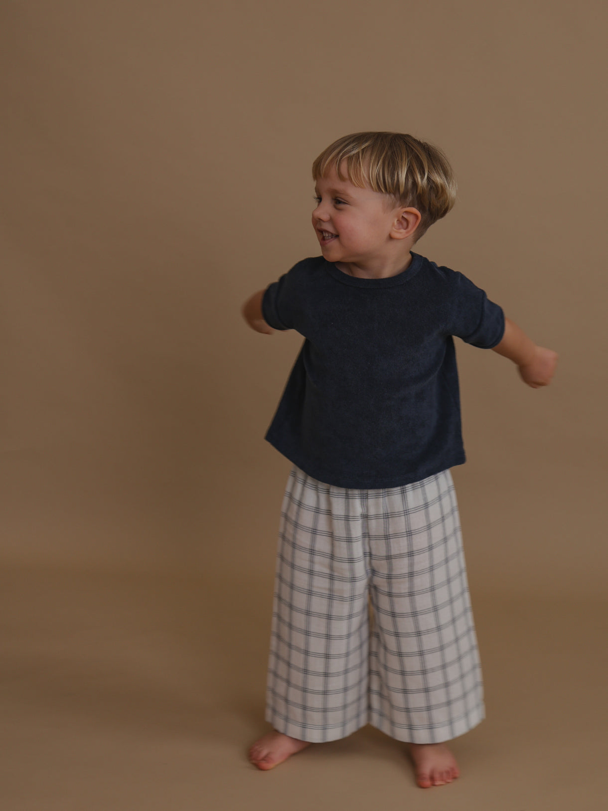 toddler wearing navy terry t-shirt & check wide leg pants swinging arms to the back