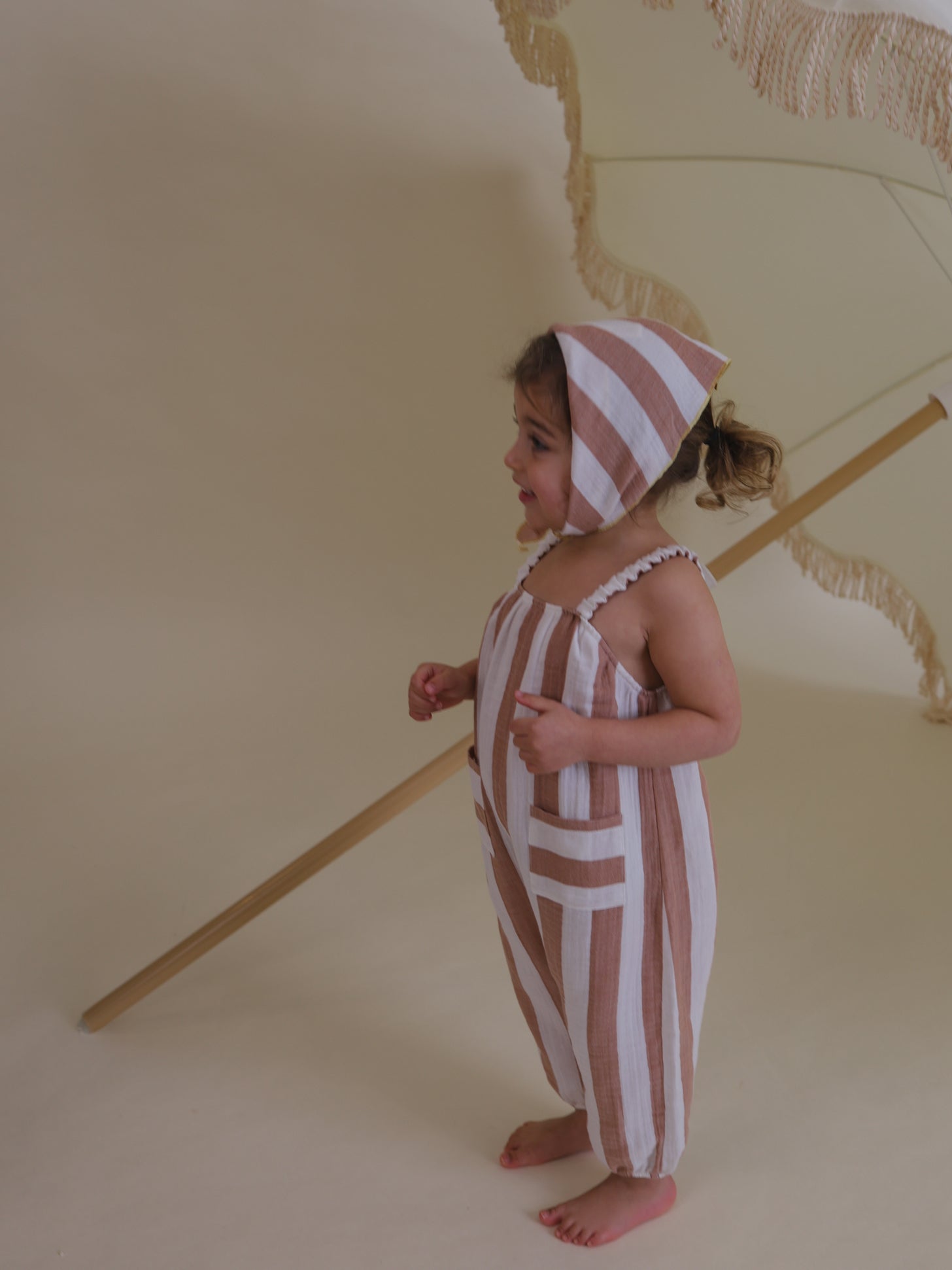 toddler in red striped soft muslin jumpsuit with gathered straps & matching scarf tied under chin
