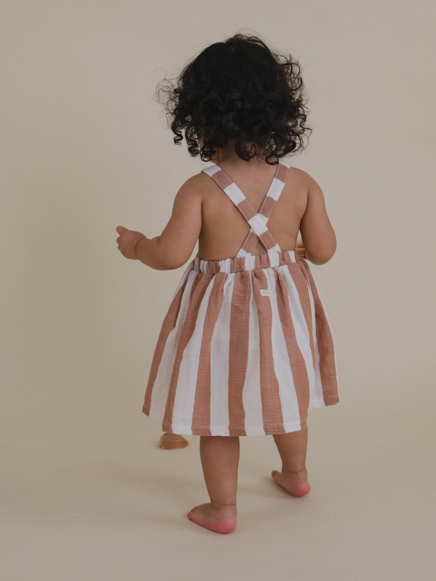 back view of toddler in sienna striped muslin apron skirt with crisscross straps & elastic waistband