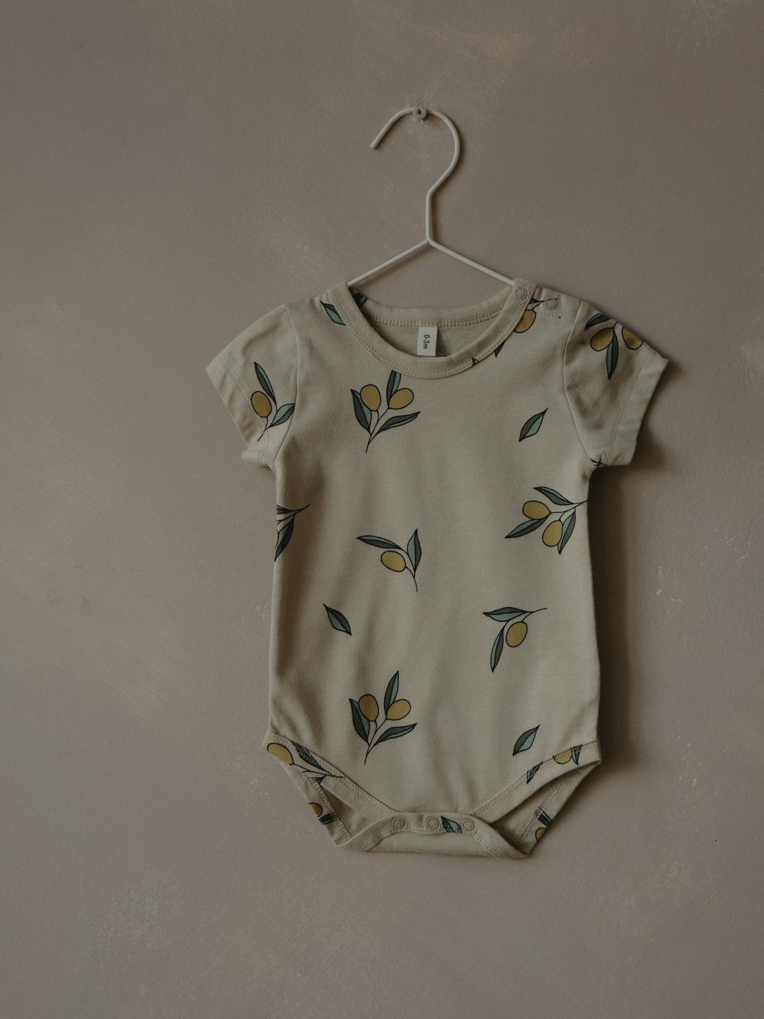 short sleeve baby bodysuit in cream with olives on hanger