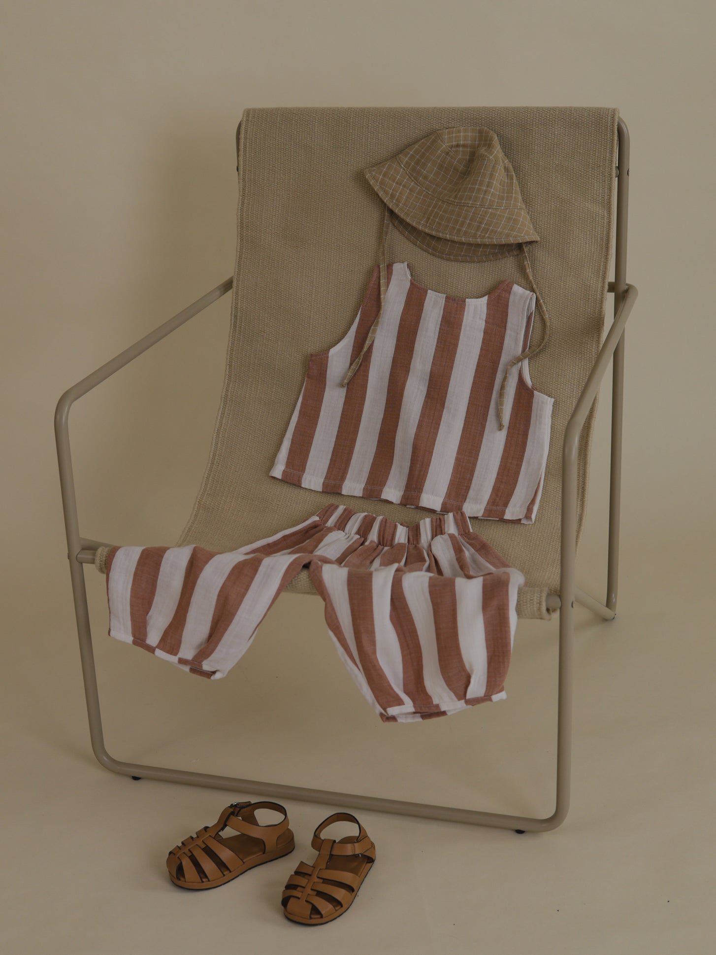 outfit flatlay on chair with sienna red striped muslin resort pants & sleeveless top set, bucket hat