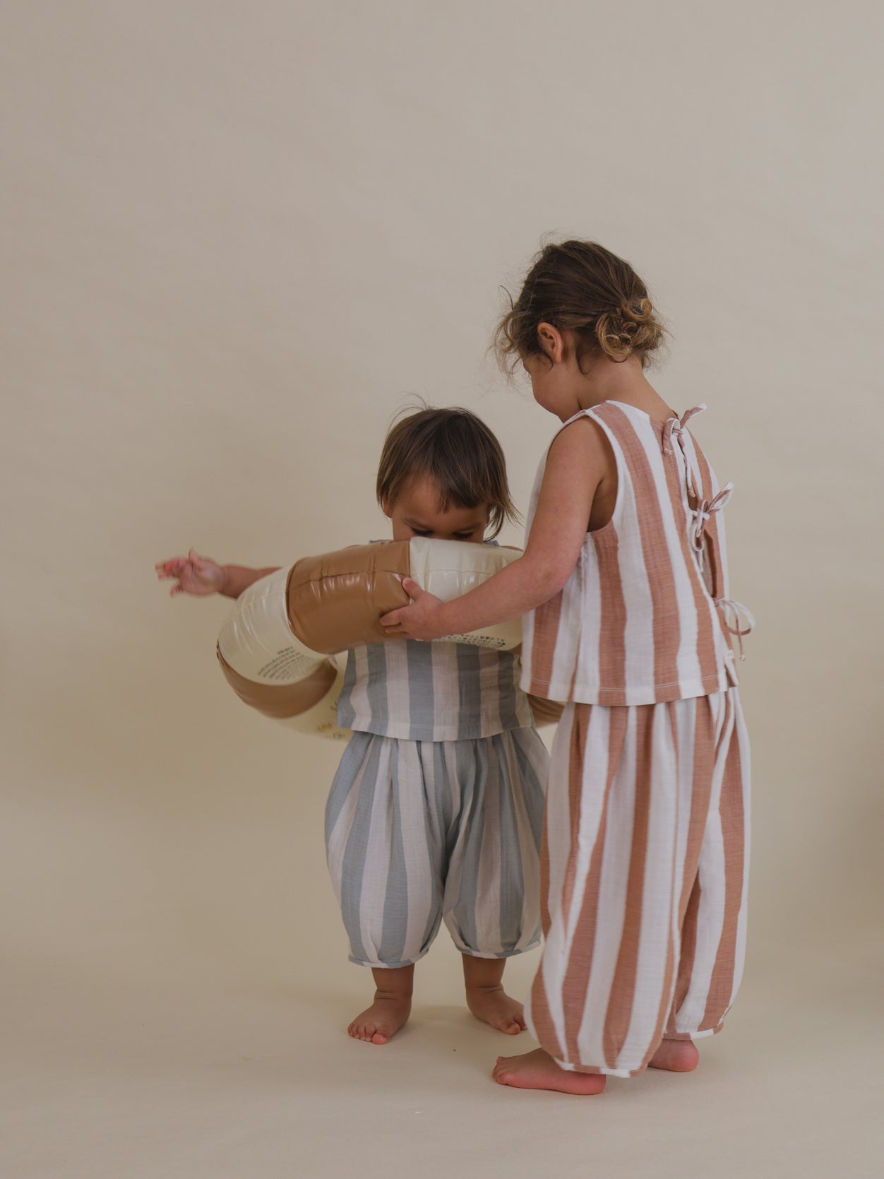 child in sienna red striped ribbon-tie back resort muslin top & pants putting pool ring on toddler