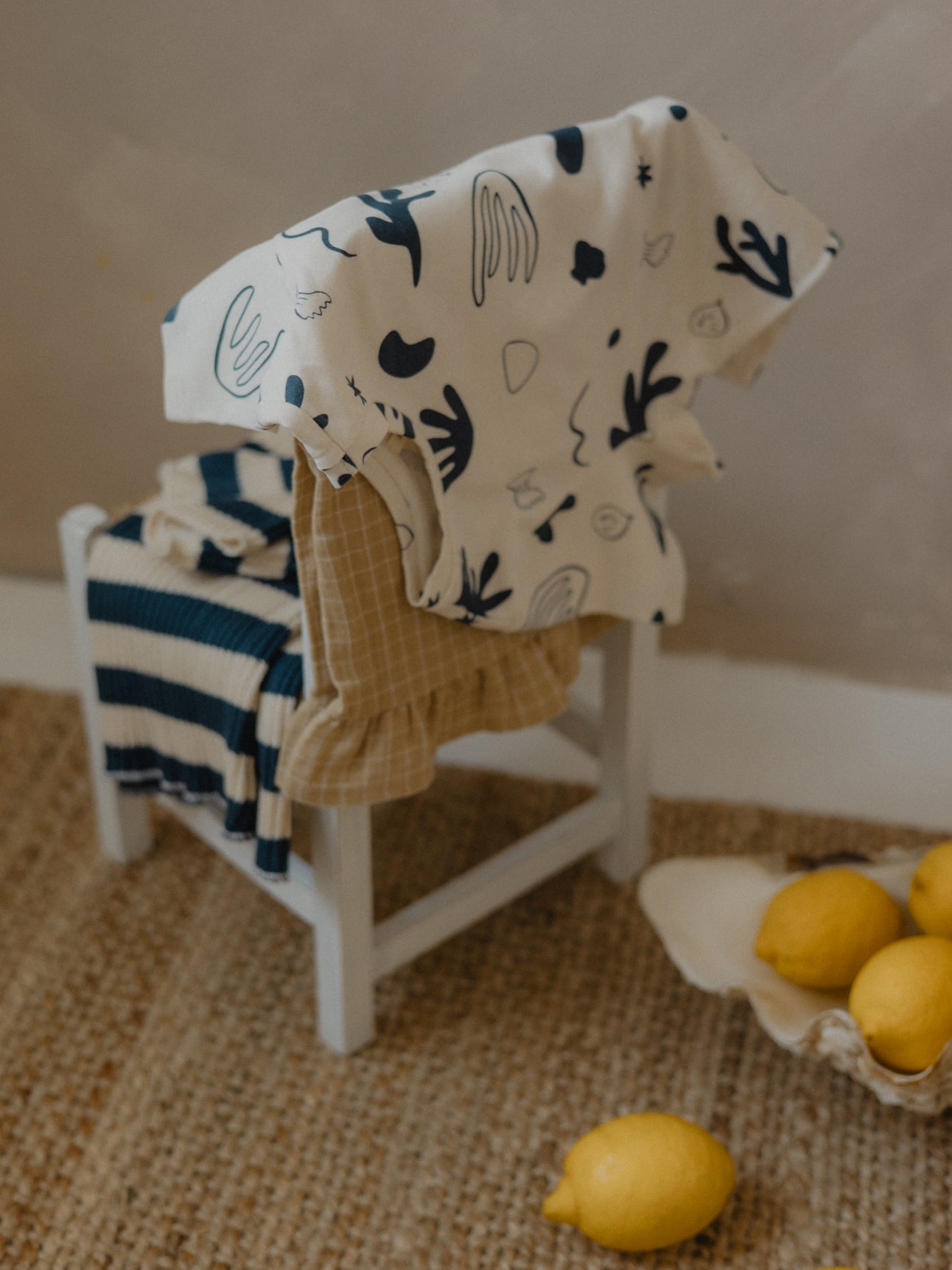 undyed cotton toddler t-shirt with ocean-inspired print draped over wooden chair back with trousers