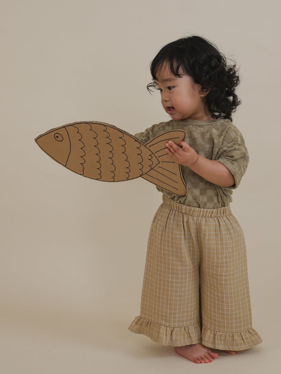toddler in lightweight muslin culottes in gold with grid check pattern playing with cardboard fish