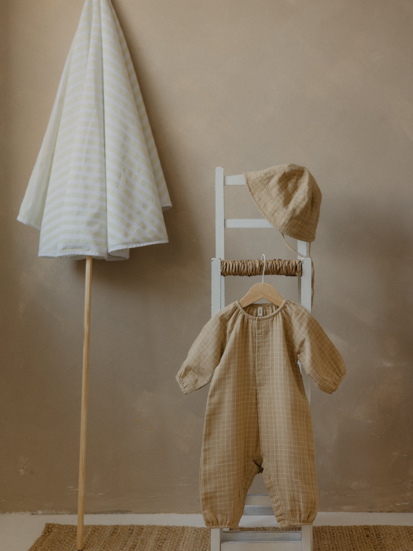 soft muslin onesie in gold with classic grid pattern & matching bucket hat hanging on chair
