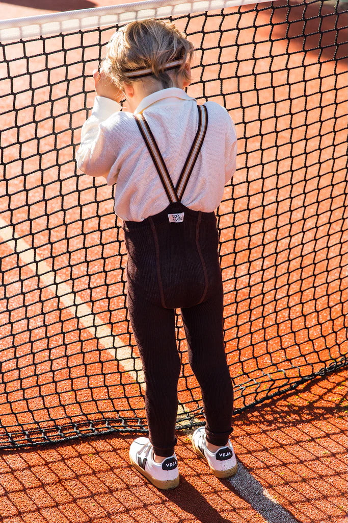 toddler wearing chocolate footless tights with contrast striped braces in tennis court playing with net