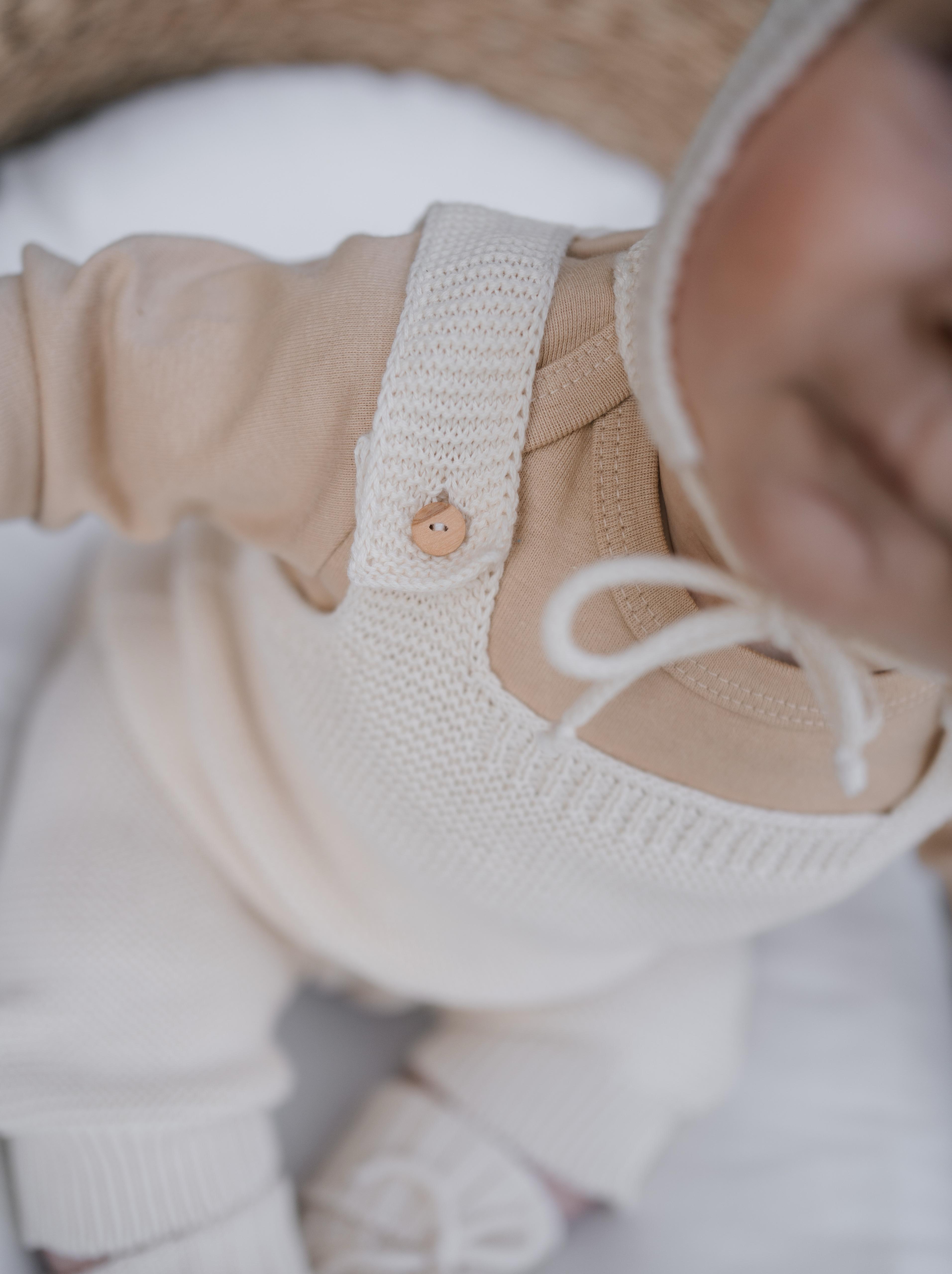 close up of baby in undyed cotton cream knitted salopette sitting in moses basket