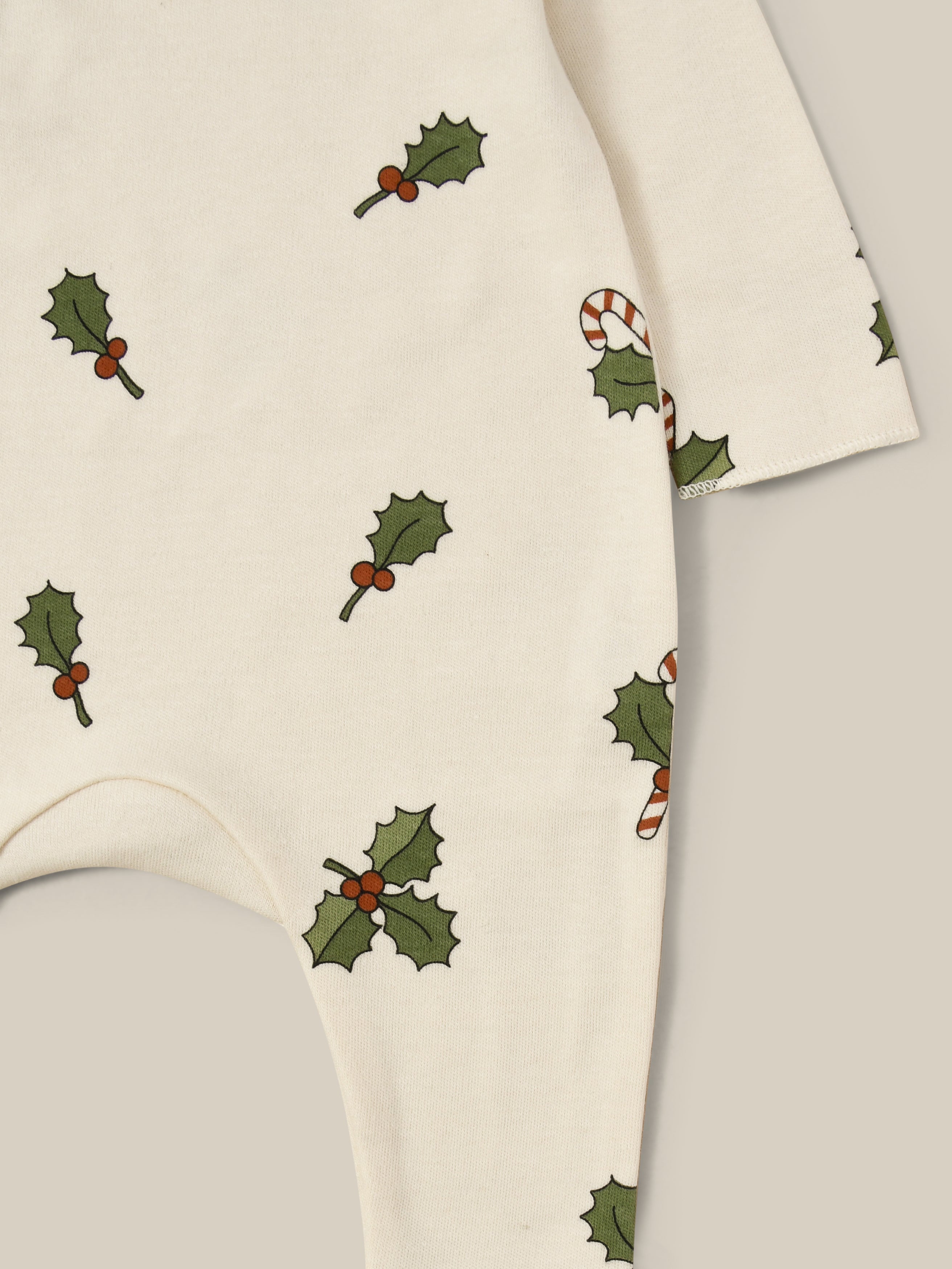 close up of christmas holly & candy cane footed sleepsuit in cream with through front poppers