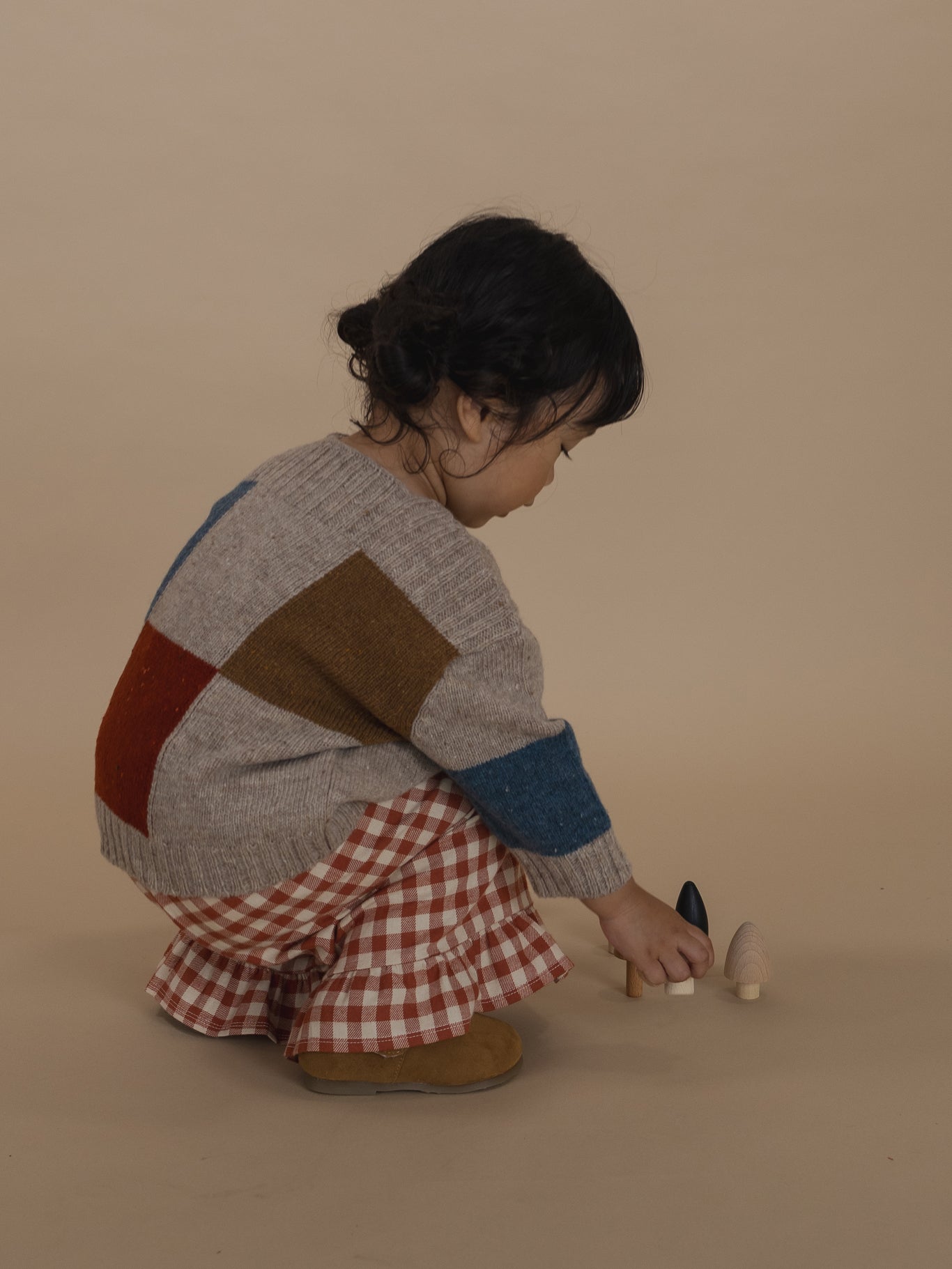 toddler in colour-block wool jumper with ribbed trims and gingham culottes, squatting and playing