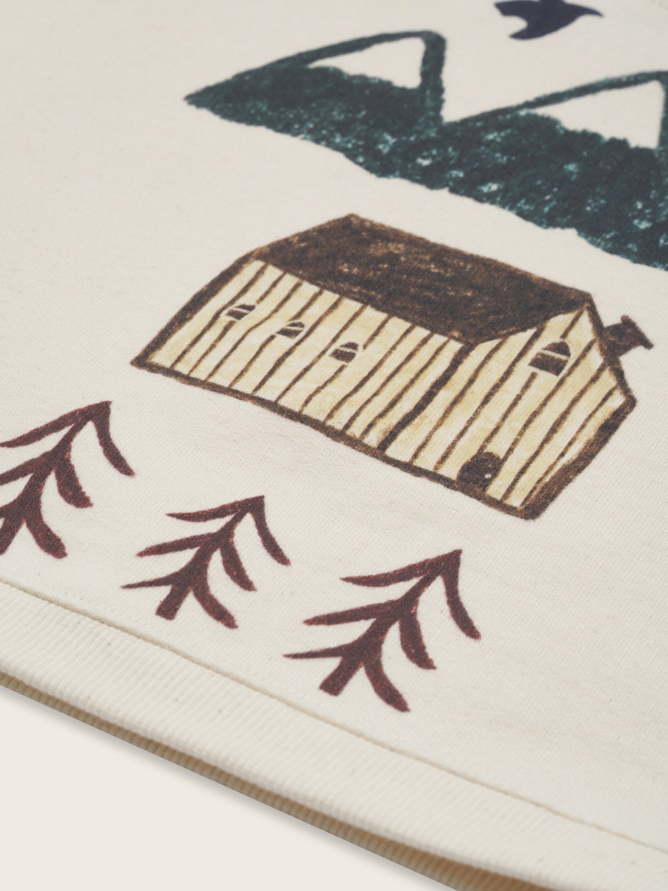 close up of cream undyed cotton sweatshirt with mountain, cabin and trees illustration on the front