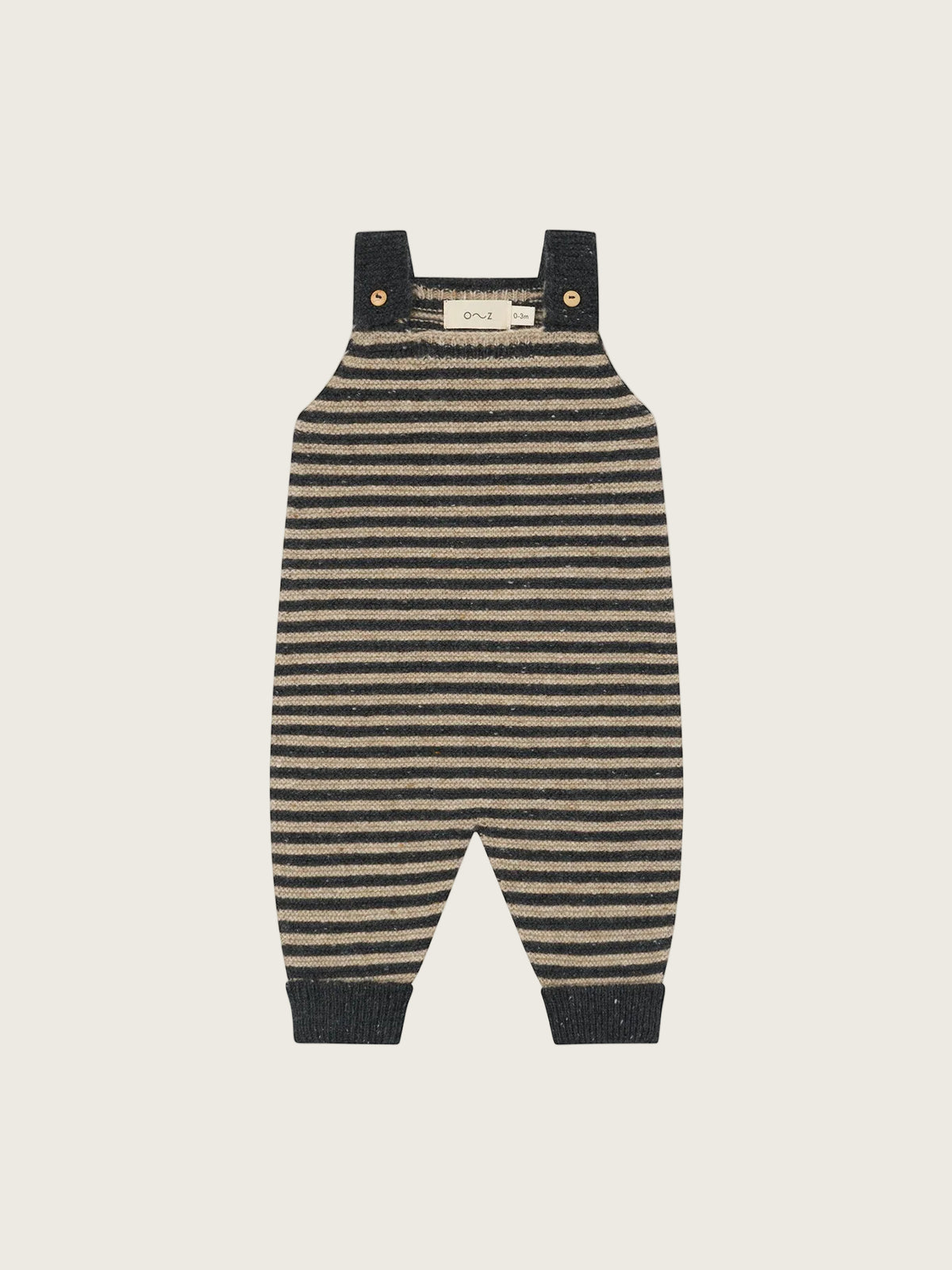 A pair of baby knit overall jumpsuit in a horizontal striped pattern of dark navy and beige, featuring dark navy shoulder straps with gold snap buttons and ribbed ankle cuffs.