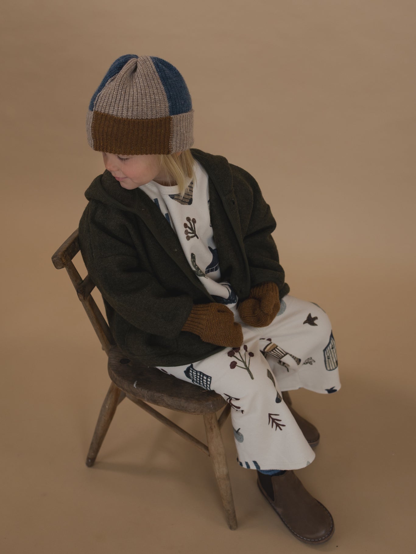 toddler in matching sweatshirt & pants, wool jacket with brown wool mittens, and patchwork beanie