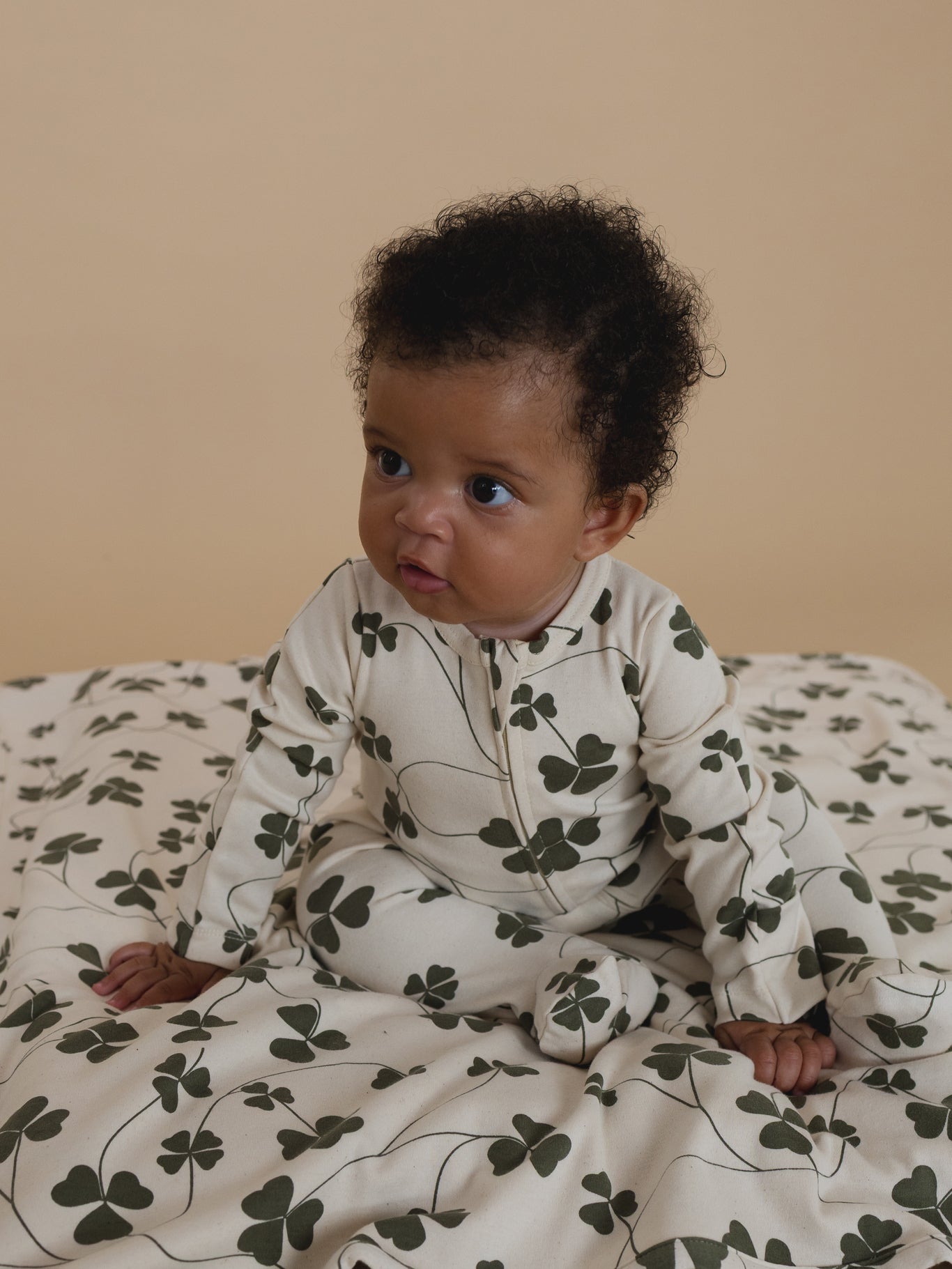 baby sitting on a blanket with green clover leaf print, with matching zip playsuit