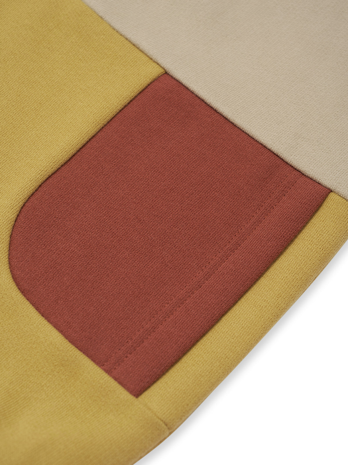Close-up of a color-blocked fabric item, showing a dusty rose patch pocket on a mustard yellow base with a light beige section on a white background.