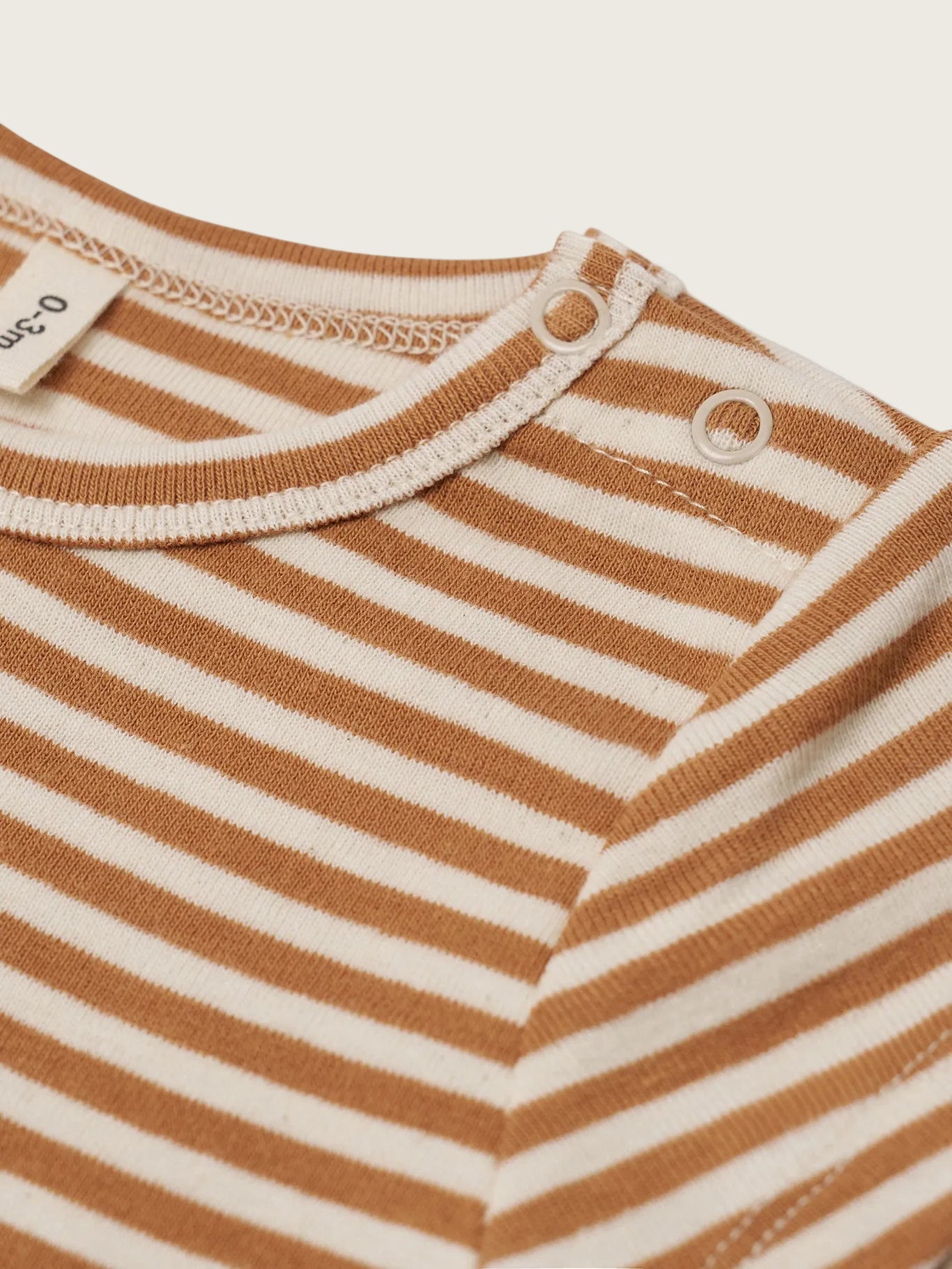 Close-up of a brown and beige striped baby outfit with a tag on a white background