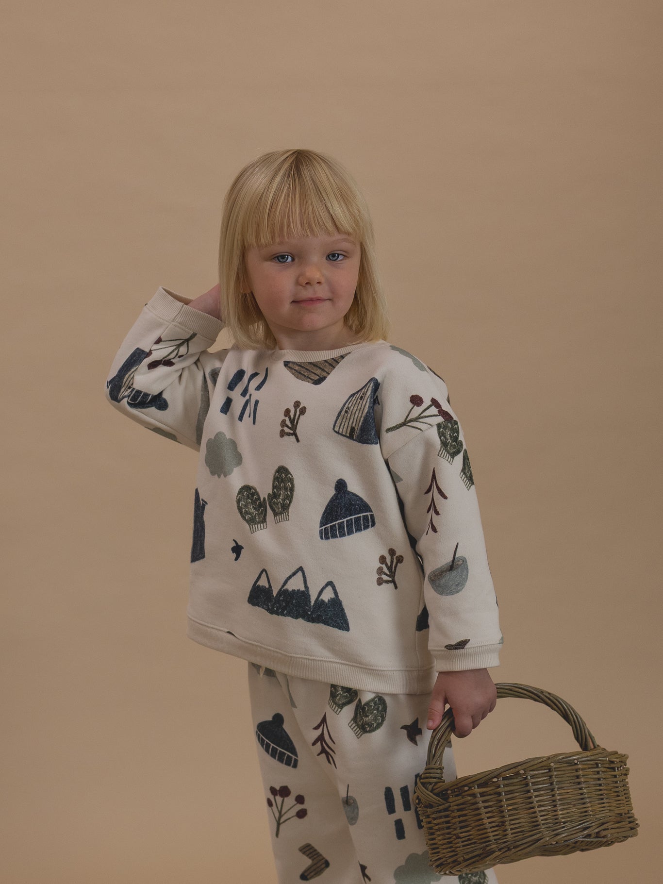 toddler in matching cream cotton sweatshirt and pants with nature-themed graphics, holding basket