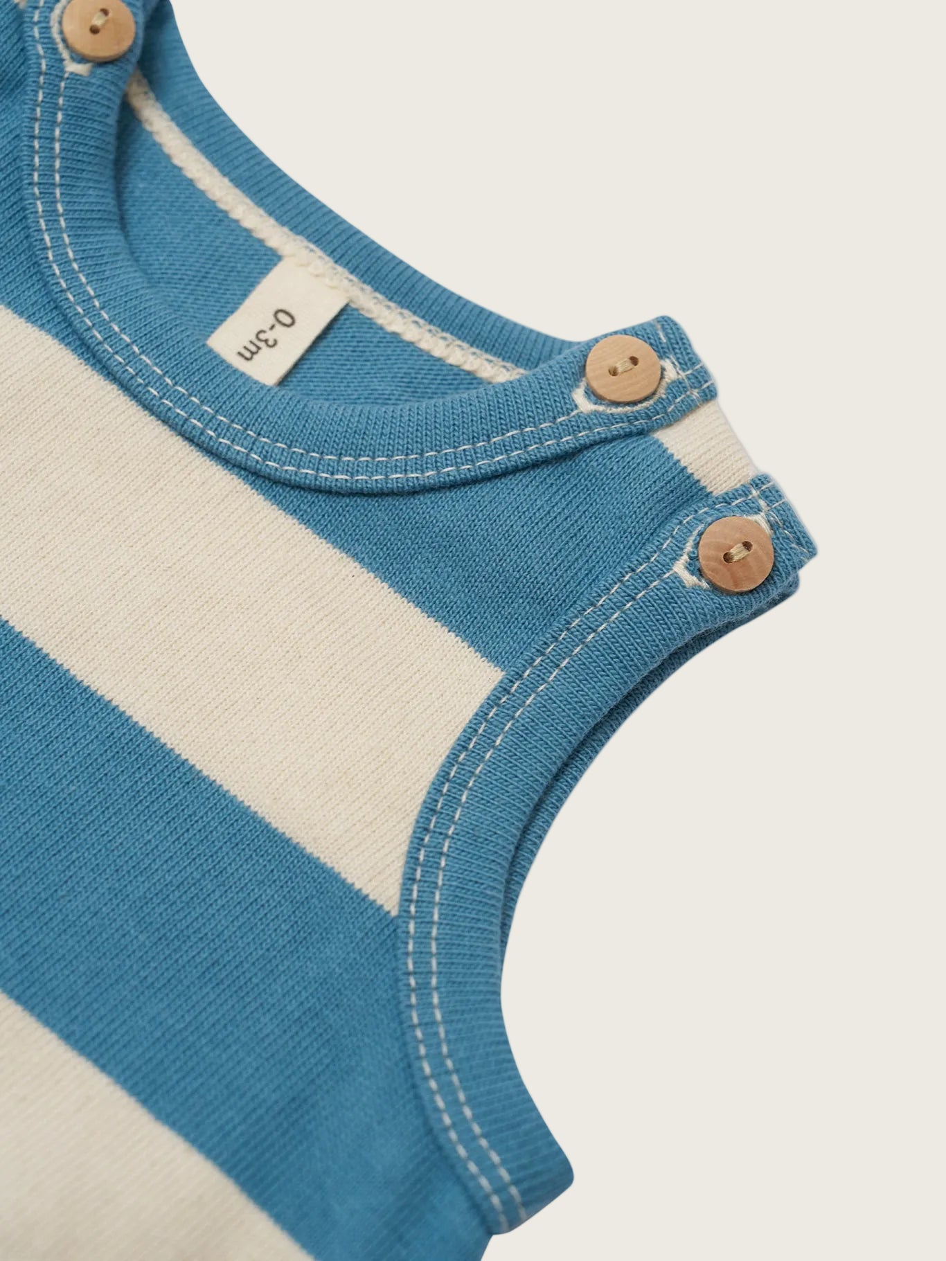 Close-up of a blue and beige baby onesie with buttons on a white background