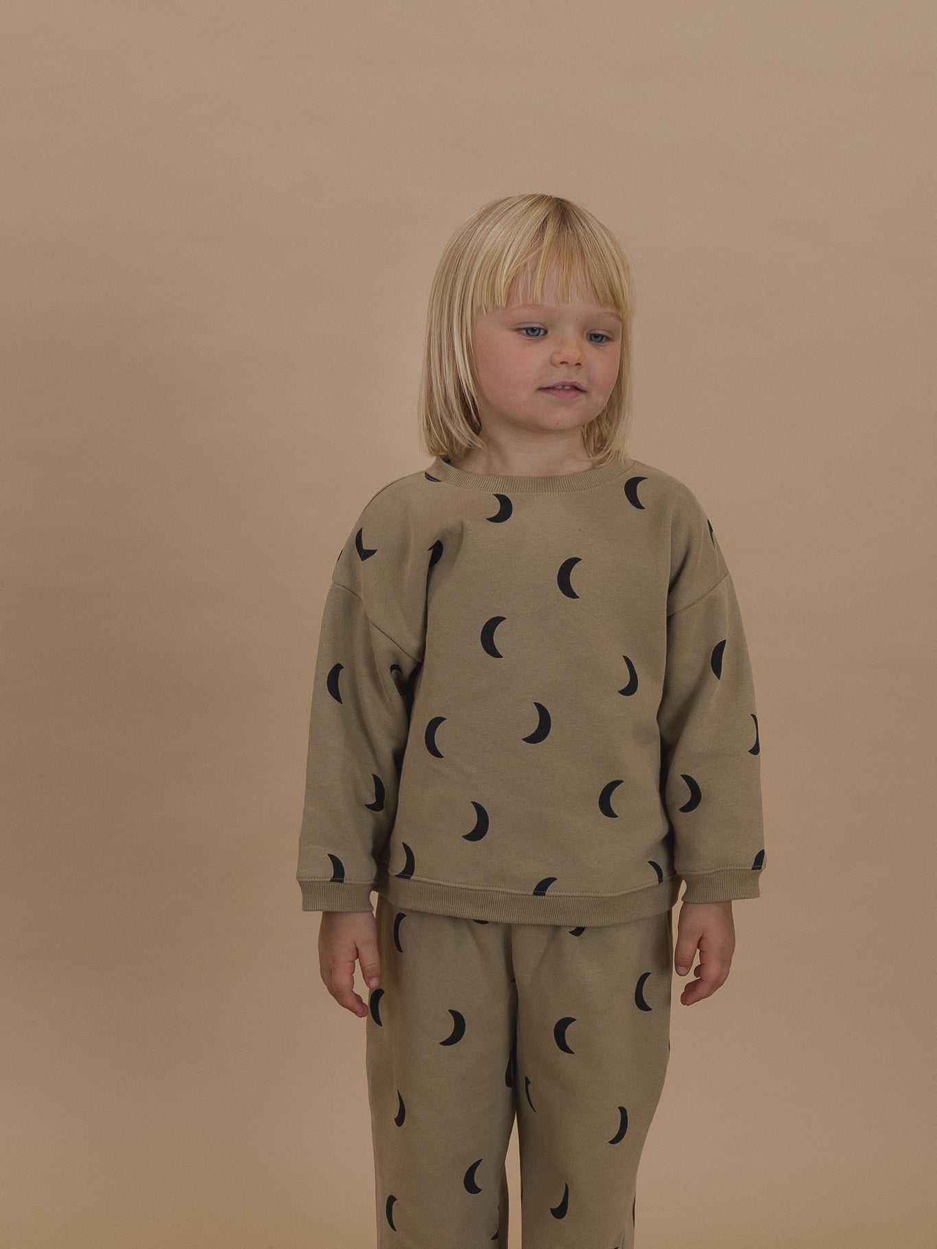 toddler in dusky beige boxy sweatshirt with black crescent moon print and matching pants