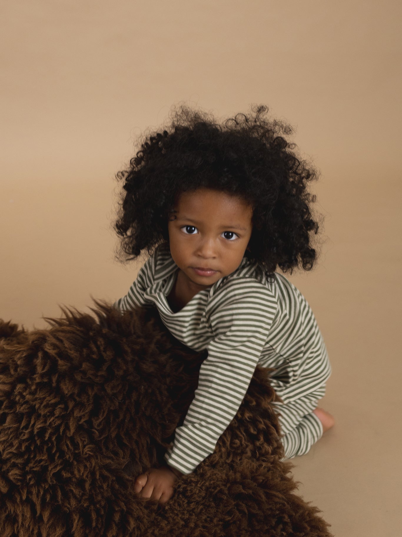 toddler in ribbed cotton long-sleeved top & leggings set in green & cream stripes, playing with rug