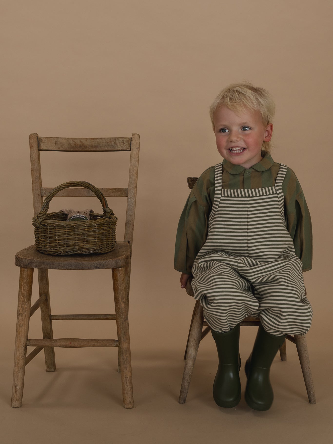 toddler in oversized green and white striped dungarees with lodge shirt sitting on wooden chair