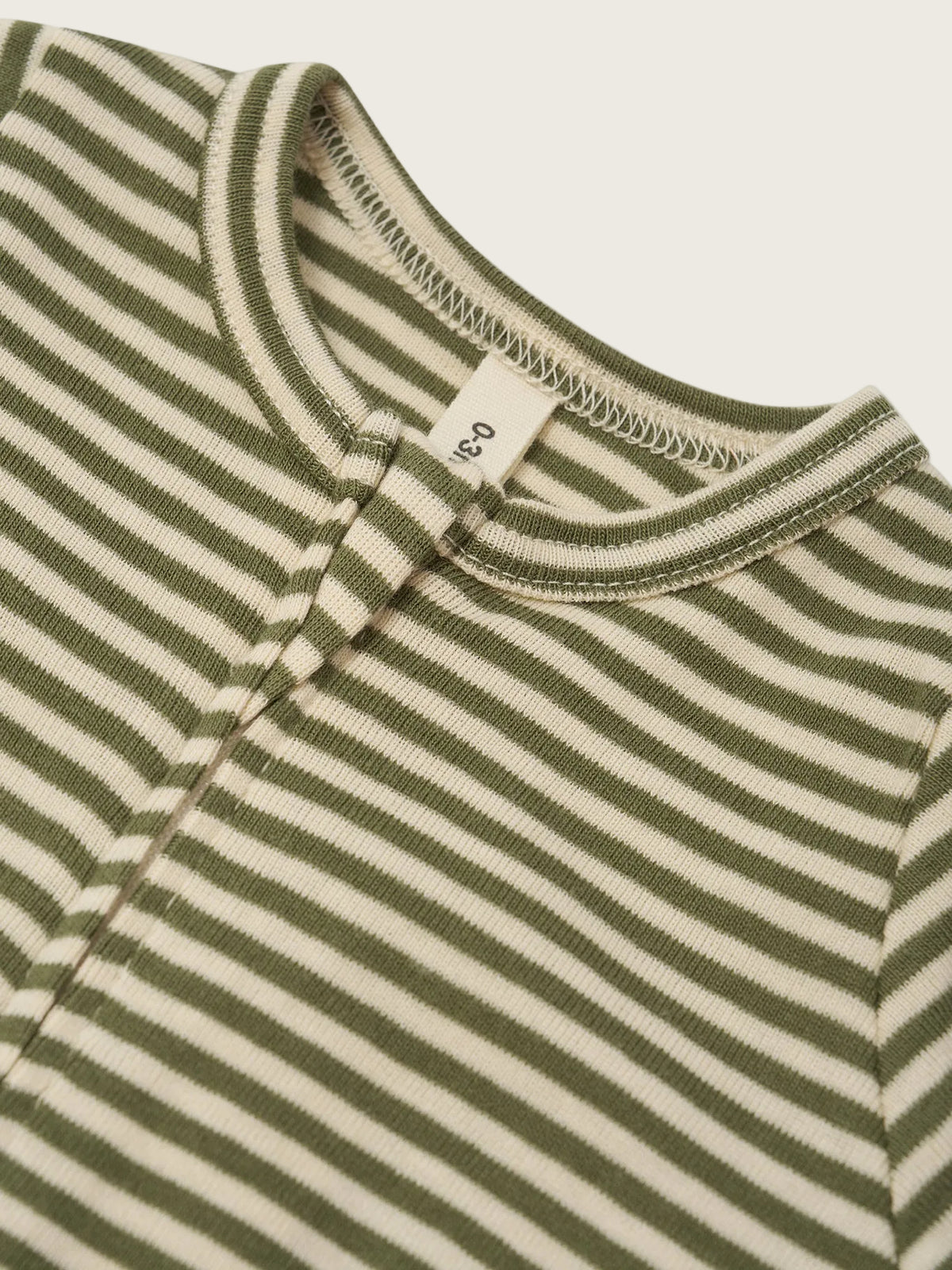 Close-up of a ribbed knit baby top with horizontal olive green and cream stripes, featuring a Henley-style collar and a small fabric size tag.