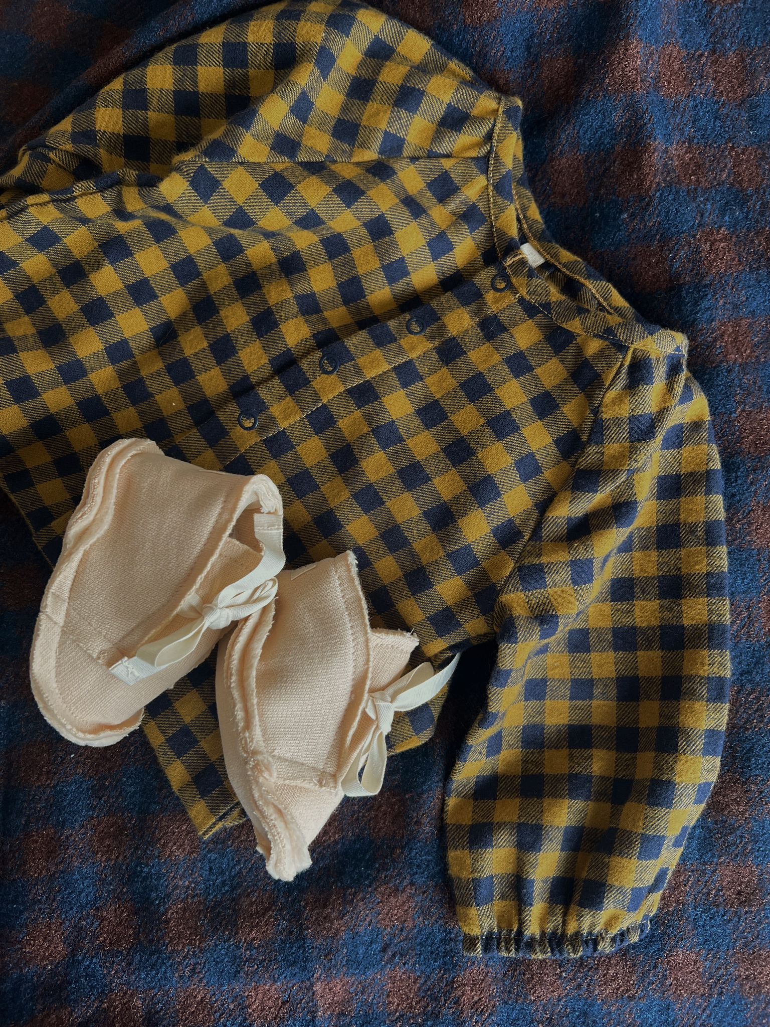 flat lay of baby pebble cotton booties on top of folded gingham flannel onesie & gingham cloth