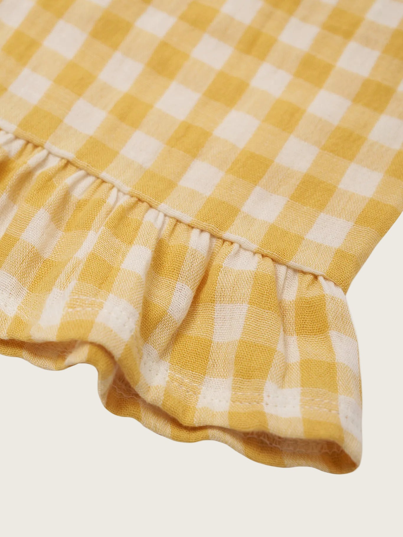 Close-up of a yellow and white checkered fabric with a ruffled edge on a white background.