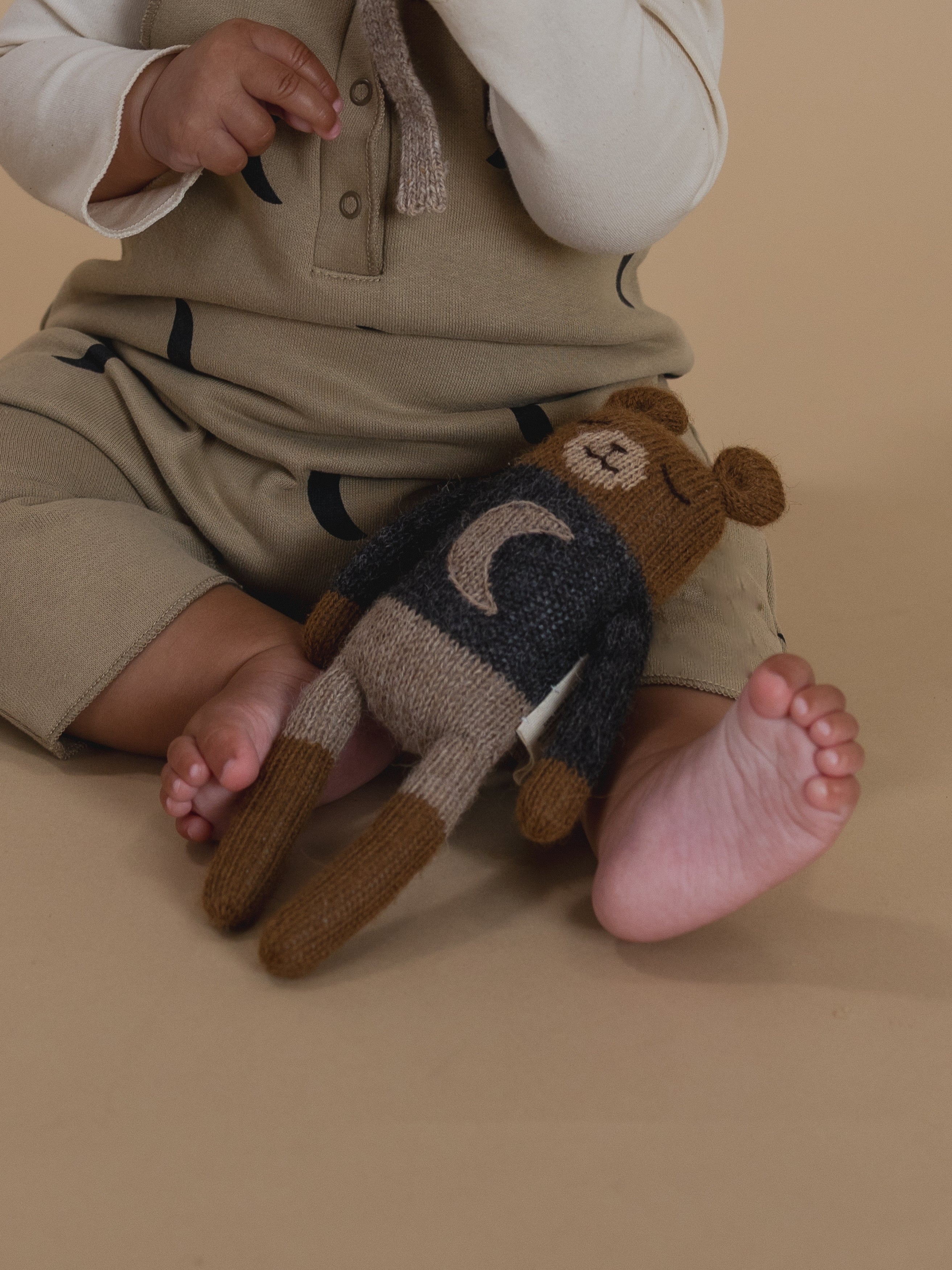 close up of knitted wool teddy toy in charcoal jumper with crescent moon motif on baby's lap