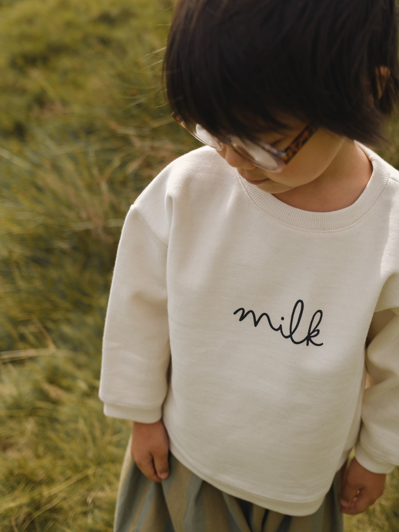 toddler in cream undyed cotton boxy drop shoulder sweatshirt with milk text standing in field