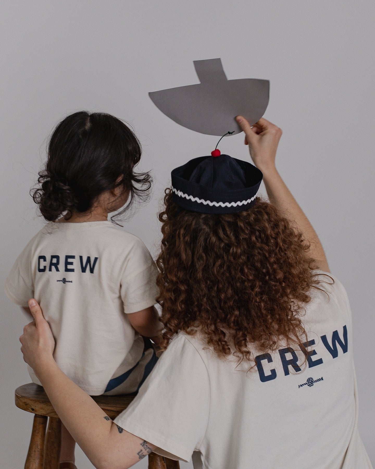 Two people wearing 'CREW' shirts with a person holding a paper ship hat.