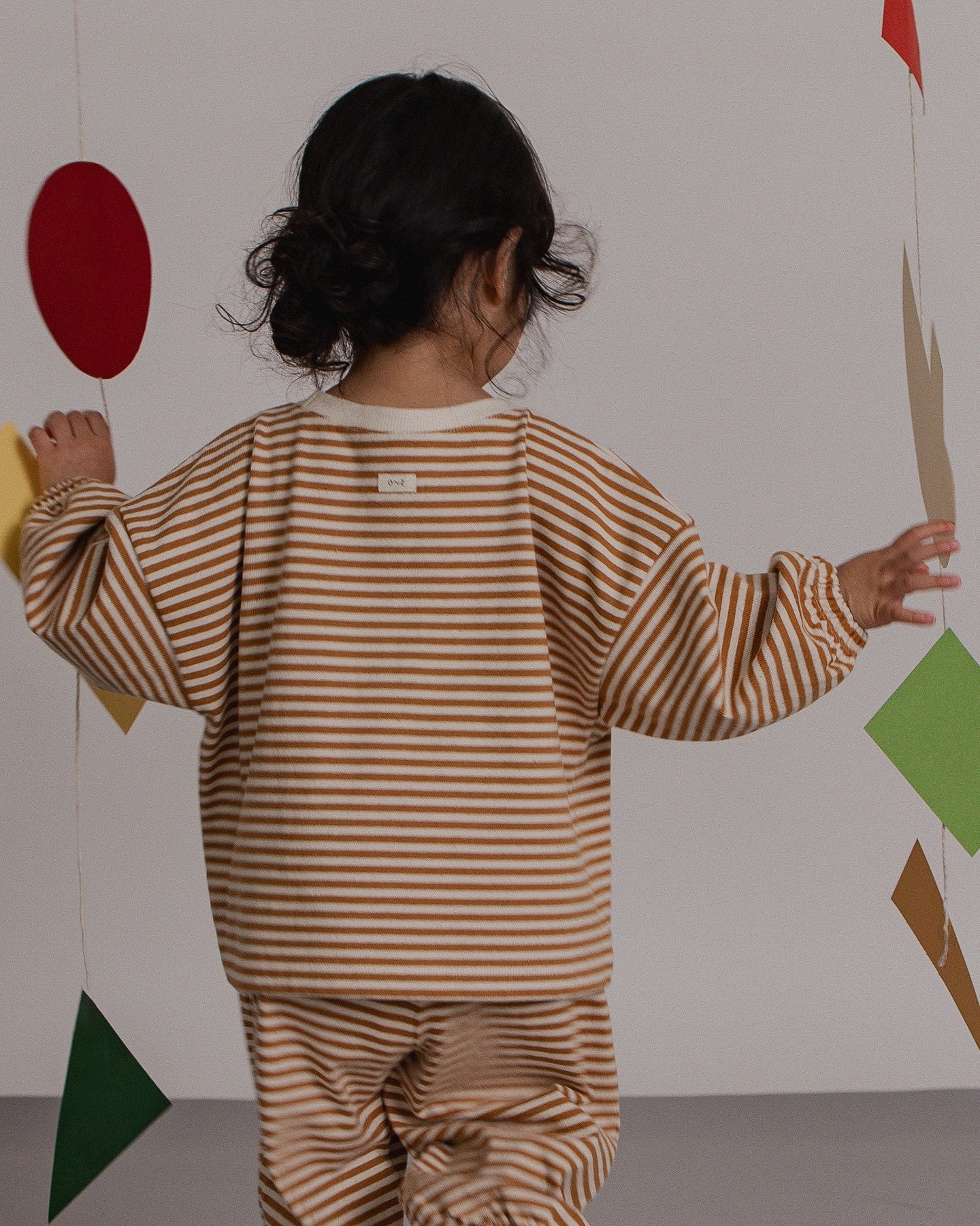 Child in a striped outfit holding colorful shapes against a plain background