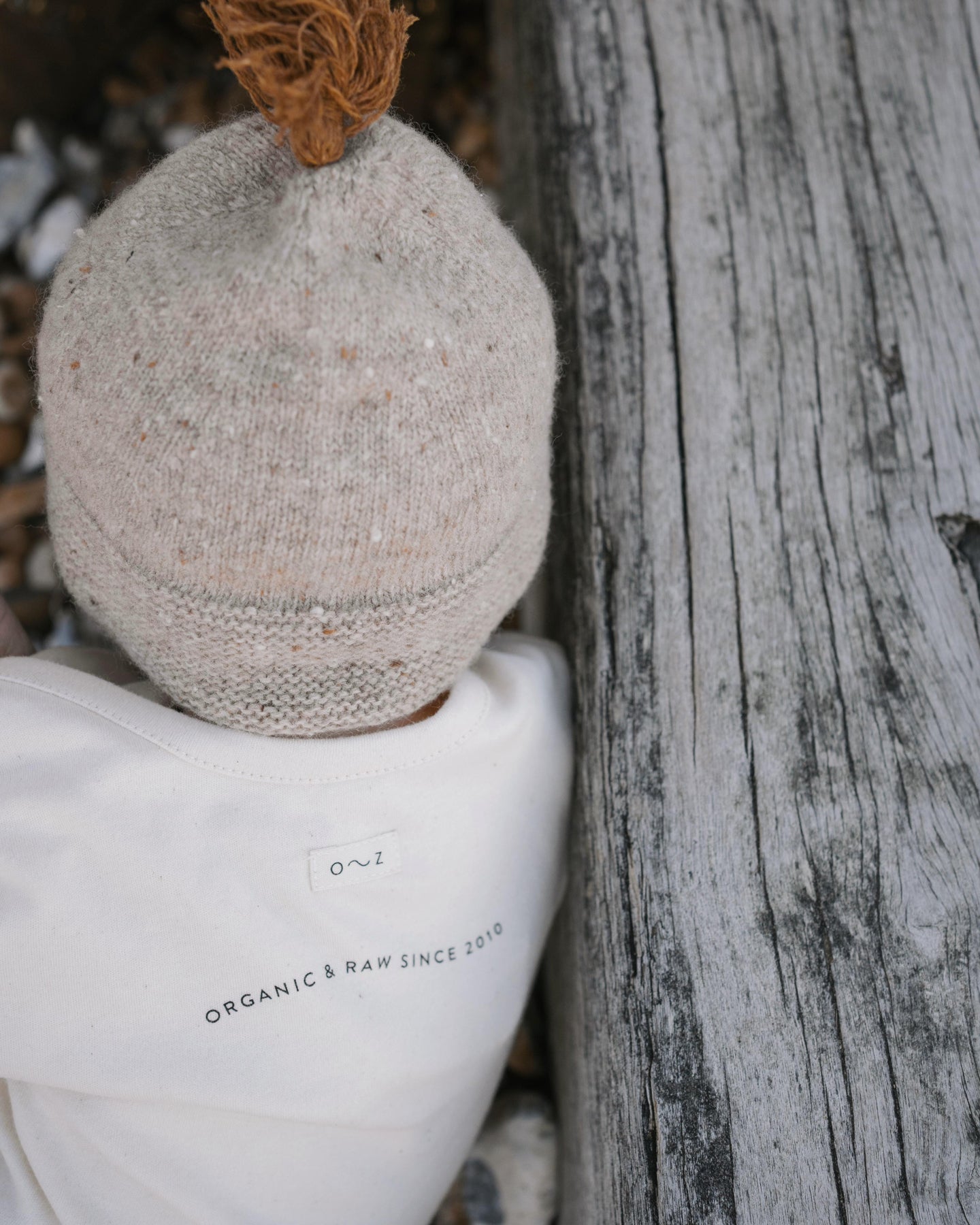 a baby in a cream undyed cotton playsuit with organic & raw since 2010 slogan