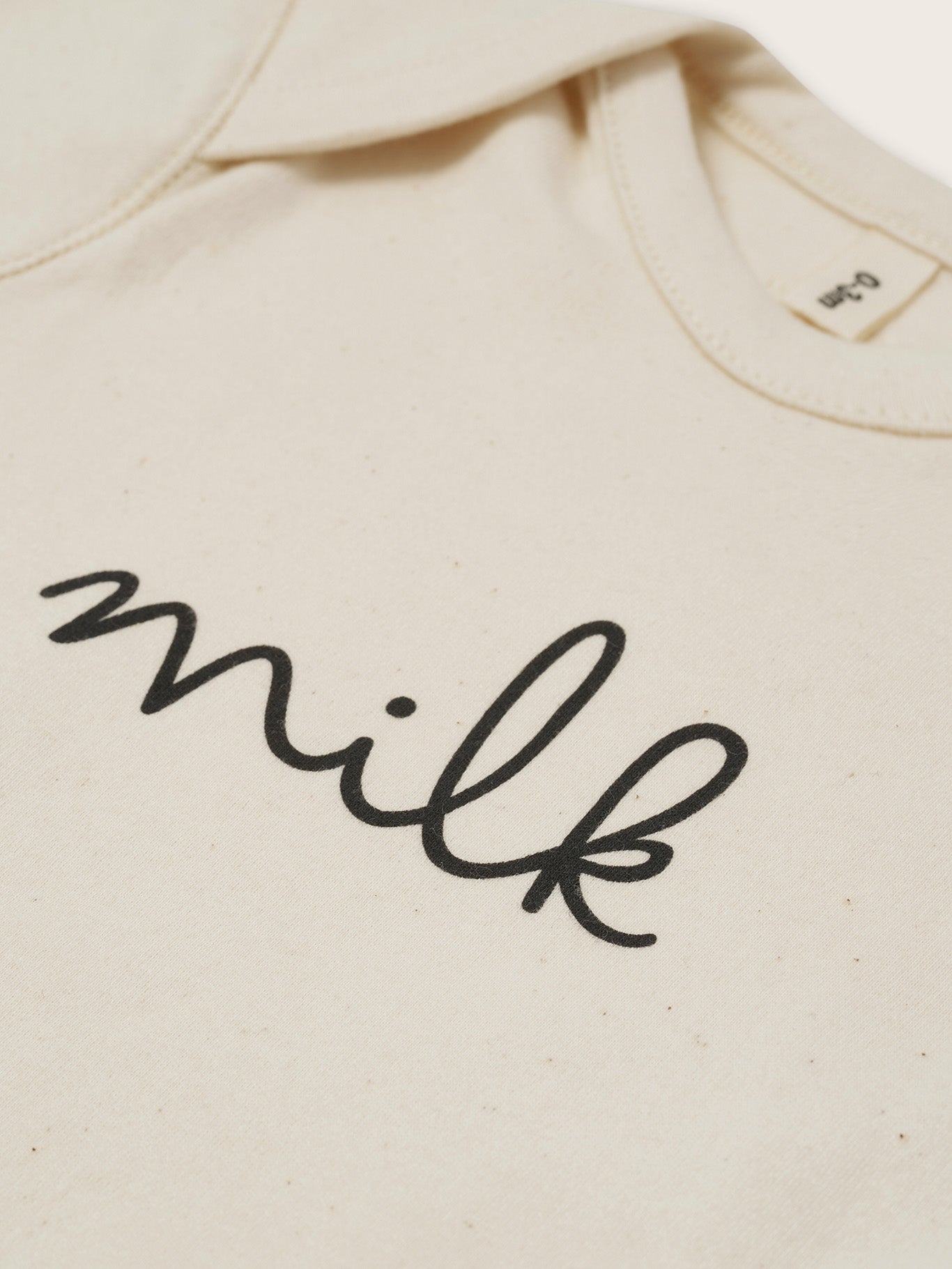 close up of baby cream undyed cotton playsuit with milk text, and envelope shoulders