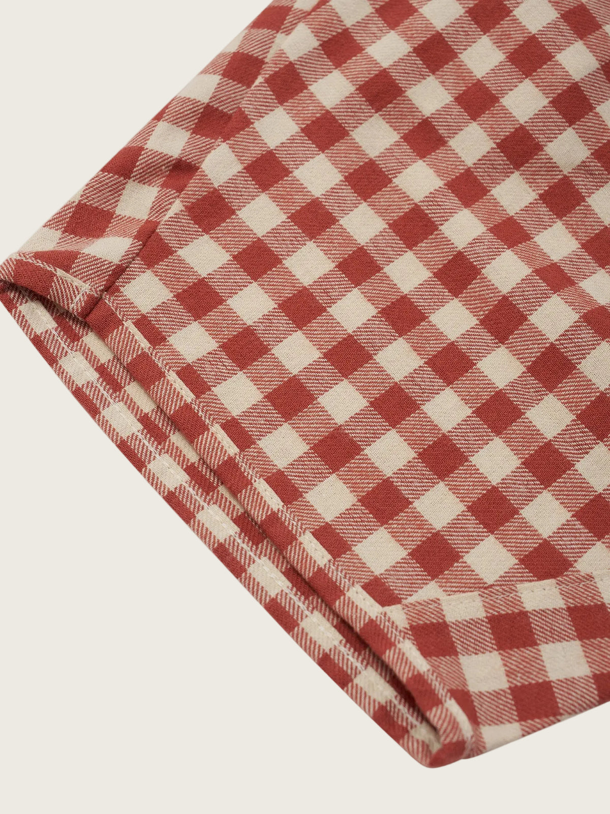 A close-up of a folded textile with a red and off-white gingham check pattern, shown against a plain light background.