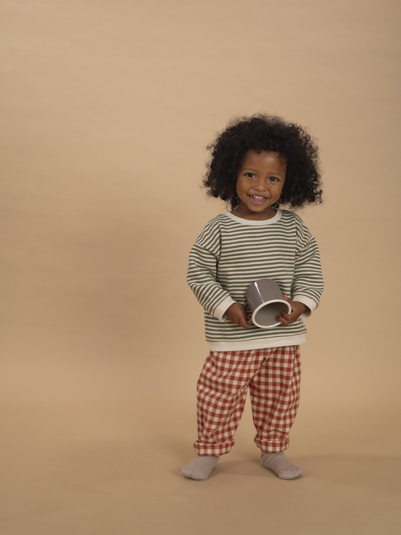 toddler in red and cream gingham wide leg flannel pants and green striped sweatshirt holding cup