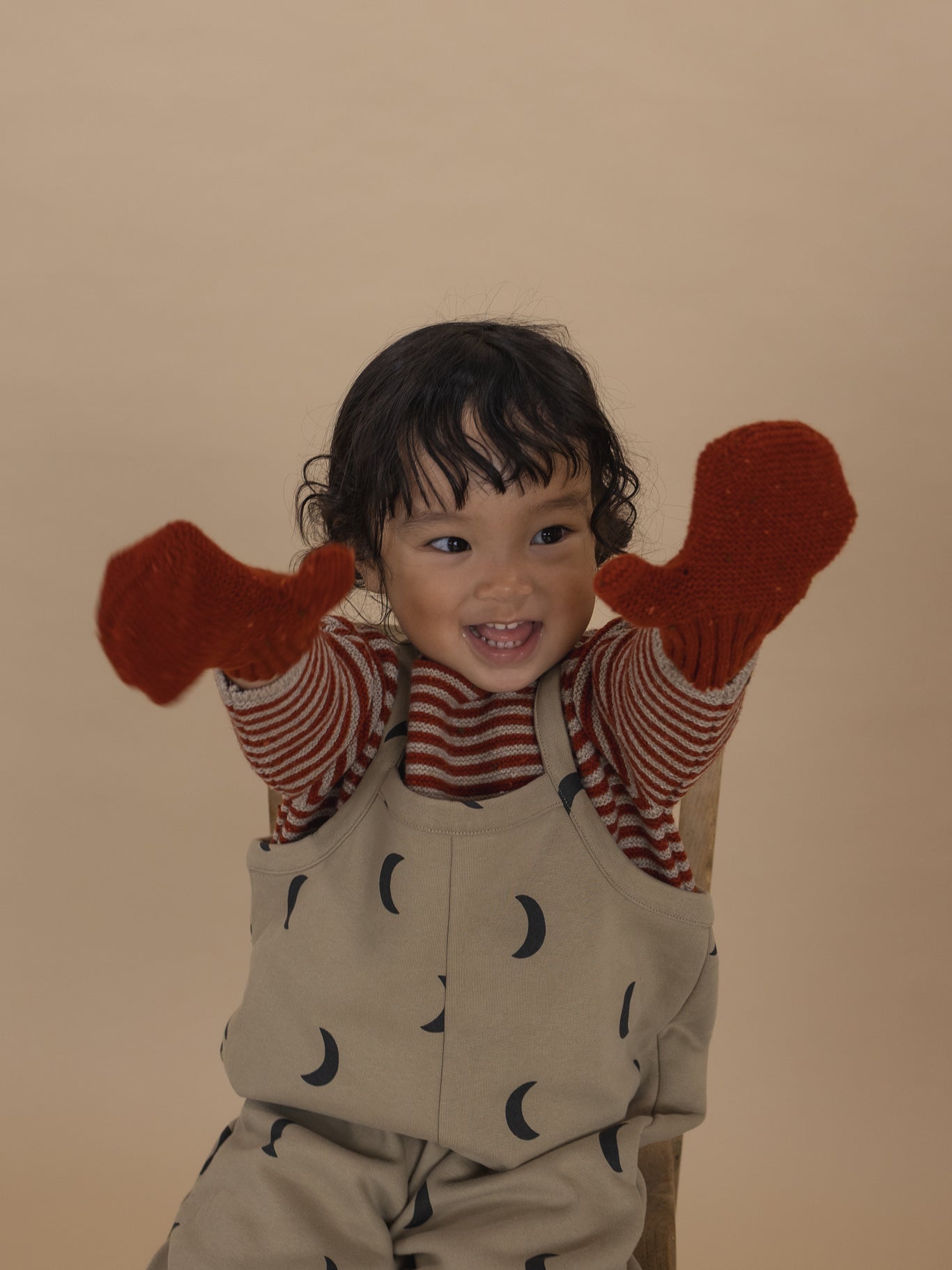 toddler in beige dungarees, paprika red wool jumper with matching knitted wool mittens