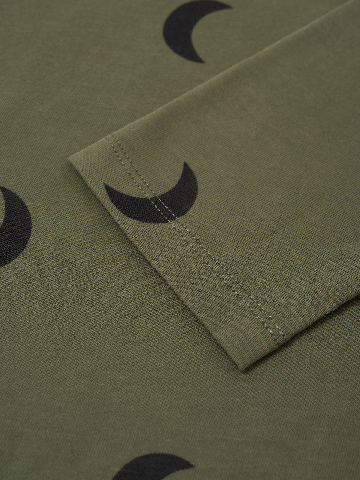 Close-up of an olive green fabric sleeve or cuff with a black crescent moon print and visible stitching.
