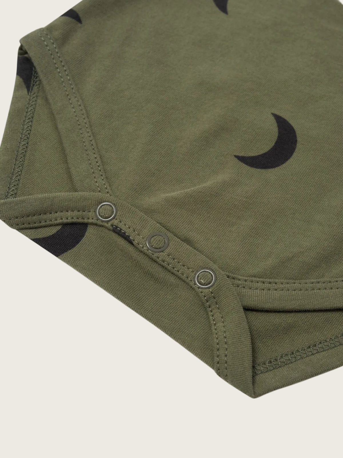 Close-up of an olive green baby garment with a black crescent moon pattern and three metal snap buttons along the neckline, shown on a white background.