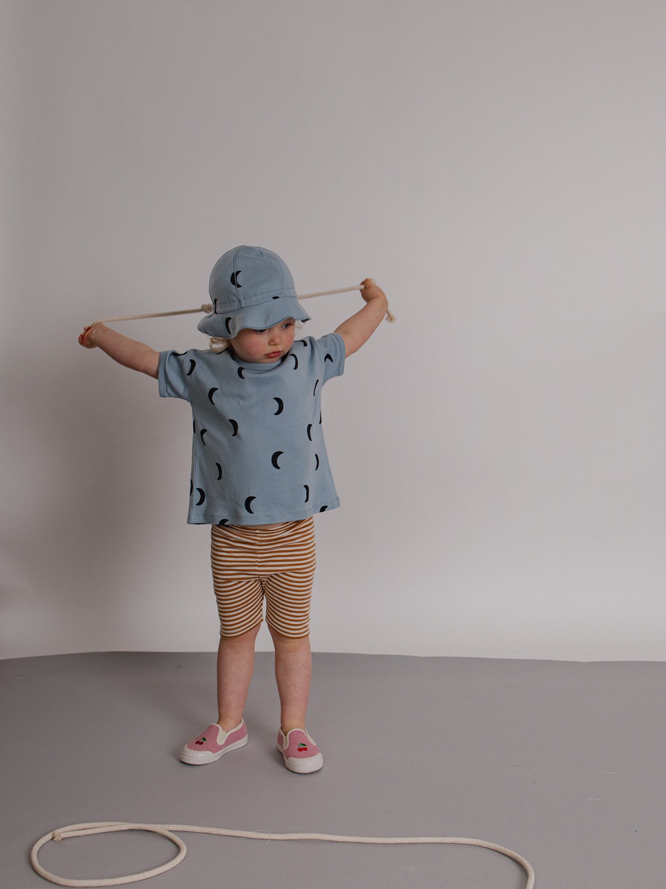 Child wearing a blue shirt with moon pattern and striped shorts, standing against a plain background.