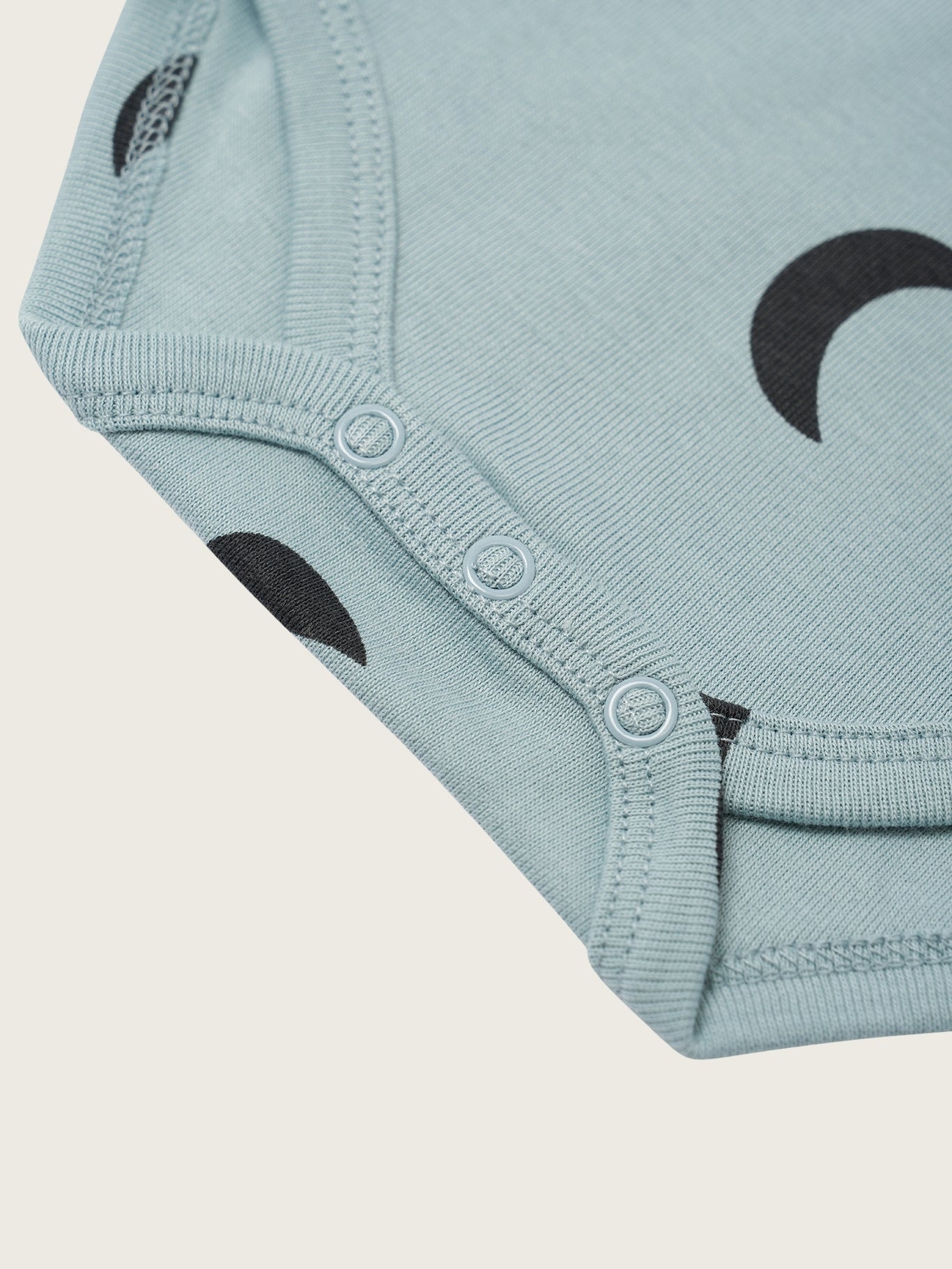 Light blue baby onesie with black cloud patterns on a beige background