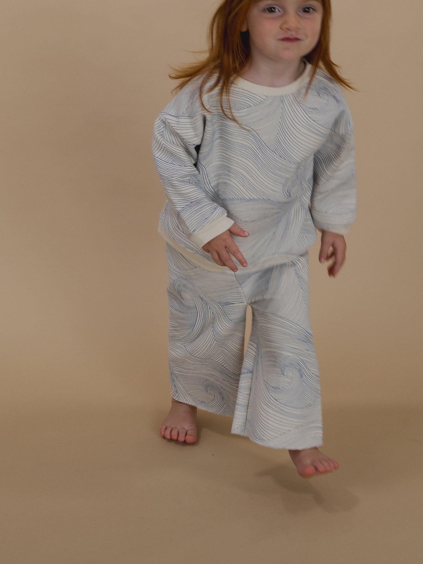 toddler in sweatshirt with blue Seascape line-drawn ocean waves and matching wide leg pants, running