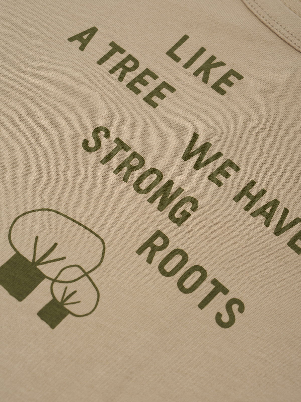 Close-up of a beige fabric surface printed with the phrase 'LIKE A TREE WE HAVE STRONG ROOTS' in dark olive green, plus a simple tree graphic.