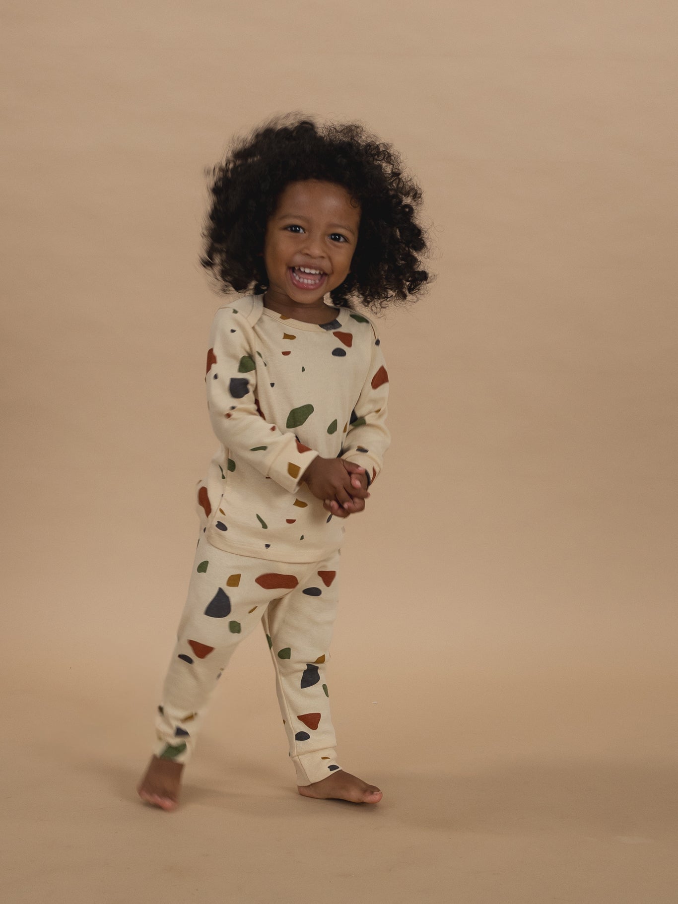 toddler in cream ribbed cotton long-sleeved top & leggings set with terrazzo print, smiling